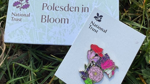 A small rectangular piece of paper with Polesden in Bloom written on it and a pin badge depicting a colourful bouquet of flowers